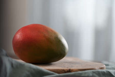 Whole ripe red mango on olive wood boardの写真素材
