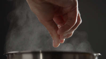 man adding salt to boiling water in saucepan with strong backlightの写真素材