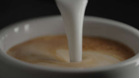 pour steamed milk into espresso in white cup closeupの写真素材