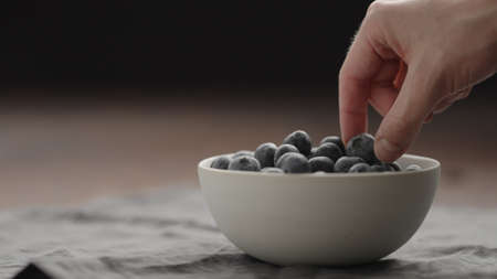 man take ripe blueberries from white bowl on walnut table with copy spaceの写真素材
