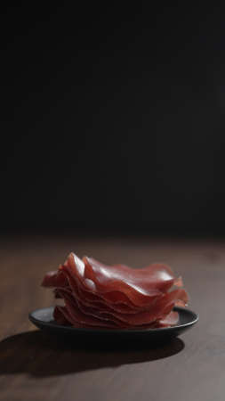vertical shot bresaola slices on saucer on walnut wood tableの写真素材