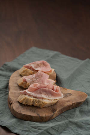 Toassted baguette slices with prosciutto cotto and cream cheese on olive wood boardの写真素材