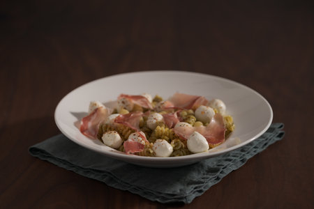 Pesto fusilli with mozzarella and coppa ham on white plate