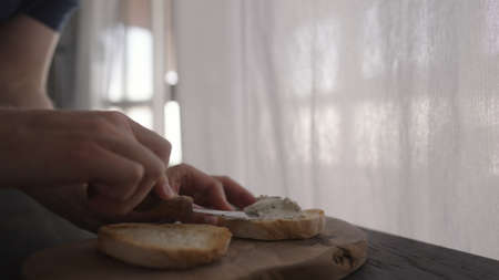 man spreading cream cheese on ciabatta to make sandwich on wood boardの写真素材