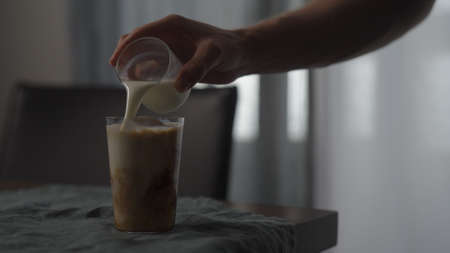 pour milk or cream in cold brewed coffee in tumbler glass with ice ball on wood table