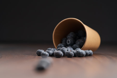 Ripe blueberries spilling from paper cup on wood tableの写真素材