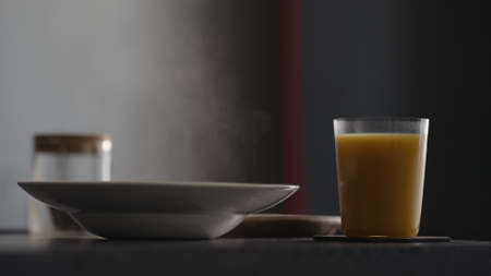 Steam rising from pasta plate with glass of orange juice on countertop
