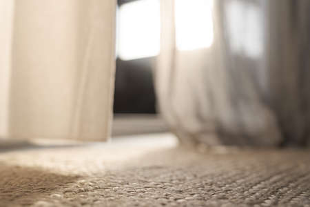 Closeup photo of jute rug on a floor with curtains on background with warm sun lightの写真素材