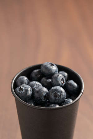 Blueberries in black paper cup on walnut tableの写真素材