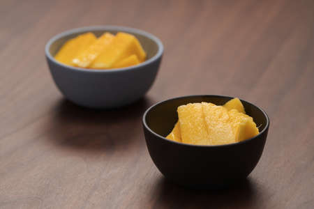 Fresh sliced mango in a ceramic bowls on walnut tableの写真素材