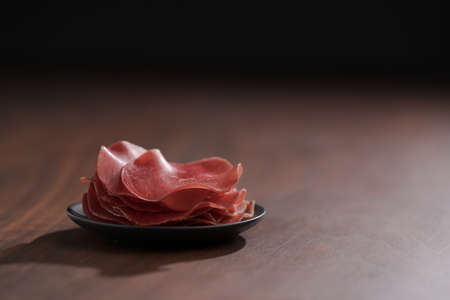 saucer with this slices of bresaola on walnut wood tableの写真素材