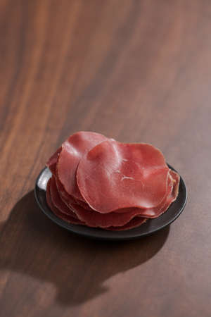 saucer with this slices of bresaola on walnut wood tableの写真素材