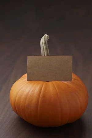 Small orange pumpkin on walnut wood table with copy space and empty paper cardの写真素材