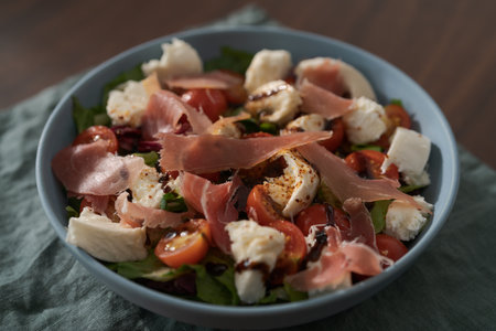 Fresh salad with prosciutto, mozzarella and cherry tomatoes in blue bowlの写真素材