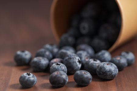 Ripe blueberries spilling from paper cup on wood tableの写真素材