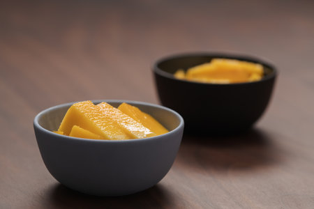 Fresh sliced mango in a ceramic bowls on walnut tableの写真素材