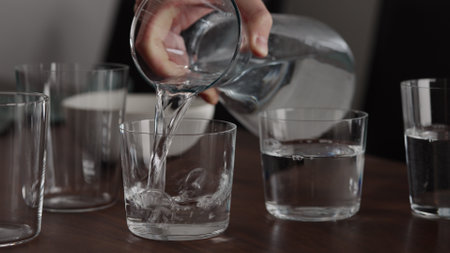Man pour water into glasses from carafe on walnut table