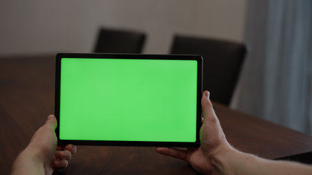 Man at home using tablet pc with green screen while sitting at the tableの写真素材