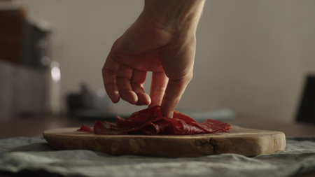man takes slices of beef pastrami from olive wood boardの写真素材