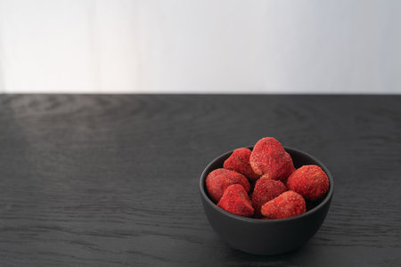 Freeze dried strawberries in black bowl on black wood tableの写真素材