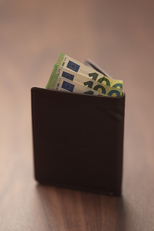 Bespoke brown all leather wallet on walnut table with euro cashの写真素材