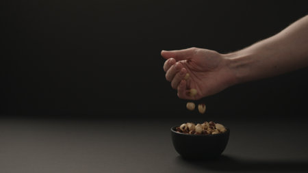 man put roasted hazelnuts into blue bowl on black paper backgroundの写真素材