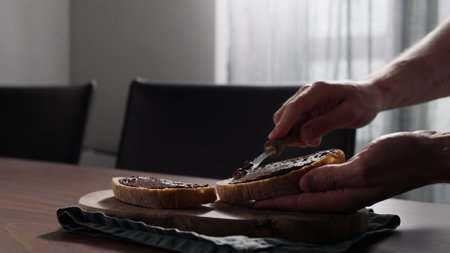 man spreading chocolate hazelnut spread on ciabatta slice on olive wood boardの写真素材