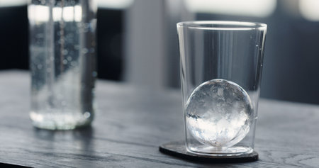 man put clear ice ball in tumbler glass on black oak tableの写真素材