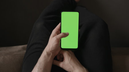 POV top view shot of man use phone with green screen indoor sitting on a couch