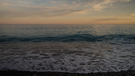 Sunset on pebble beach with sea waves of mediterranean seaの写真素材
