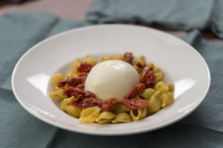Pesto conchiglie with sundried tomatoes and burrata cheese served in white plateの写真素材
