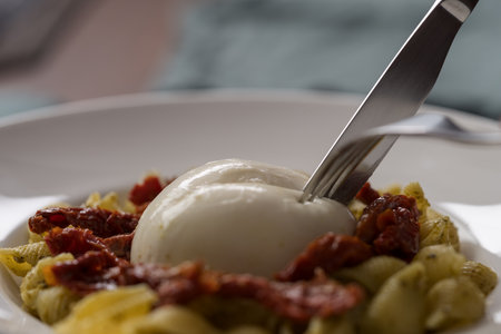 Closeup of pesto conchiglie with sundried tomatoes and cutting burrata cheese served in white plateの写真素材