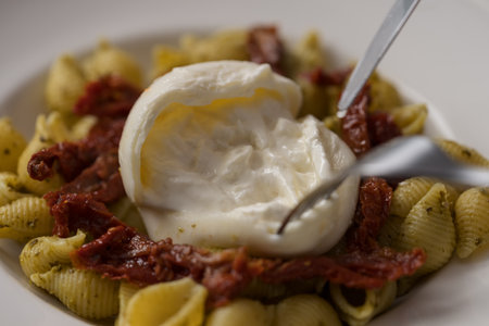 Closeup of pesto conchiglie with sundried tomatoes and cutting burrata cheese served in white plateの写真素材