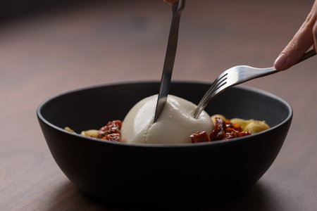 Closeup of pesto conchiglie with sundried tomatoes and cutting burrata cheese served in black bowlの写真素材