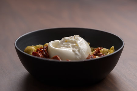 Pesto conchiglie with sundried tomatoes and burrata cheese served in black bowlの写真素材