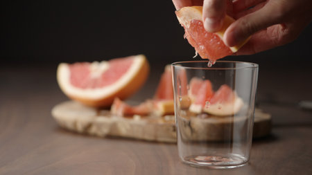 man squeeze grapefruit into tumbler glass on wood tableの写真素材
