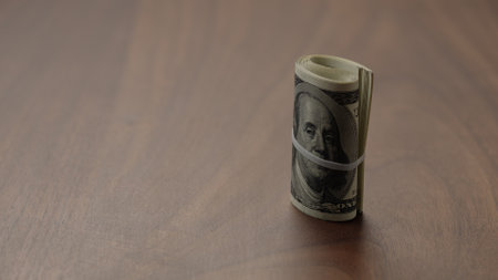 Roll of hundred dollar bills on walnut table shotの写真素材