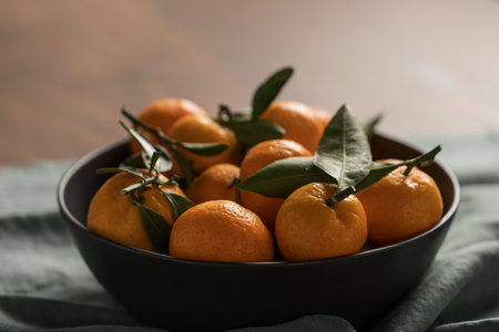 Small organic tangerines with leaves in ceramic bowl on wood tableの写真素材
