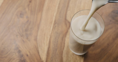 pour oat milk in glass on wood background with copy space