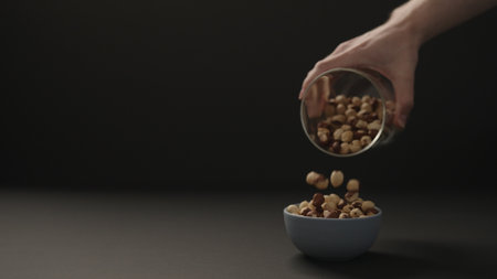 man pour roasted hazelnuts into blue bowl on black paper background