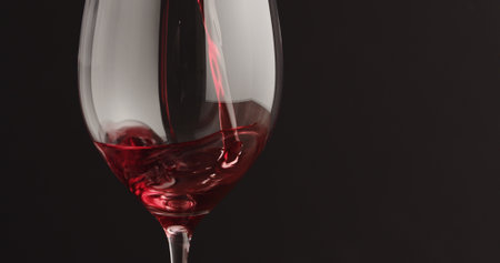 pour red wine into wineglass over black baground