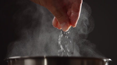 man adding salt to boiling water in saucepan with strong backlight
