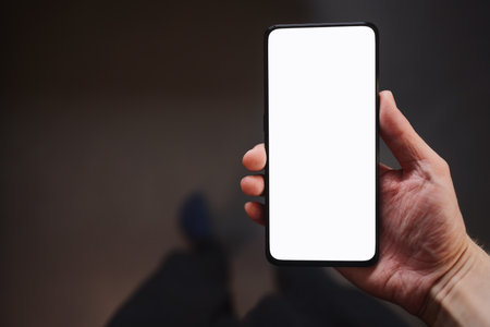 Man hold smartphone with white screen in his hand standing indoors in home environmentの写真素材