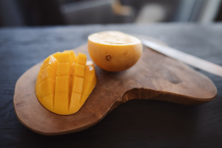 Cut in halves thai yellow mango on olive wood boardの写真素材