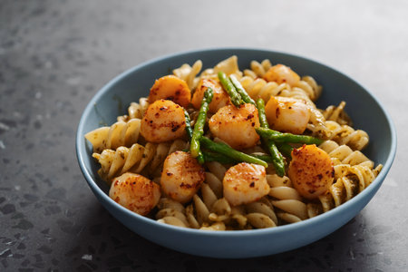 Fusilli pasta with scallops and asparagus in blue bowl on concrete surfaceの写真素材