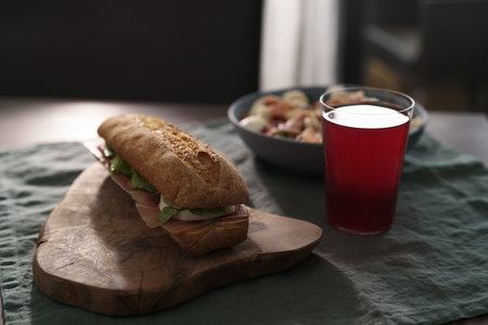 Baguette sandwich with jamon, mozzarella and salad leaves with bowl of salad and glass of lemonade for lunch on dining tableの写真素材