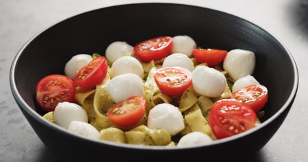pesto fettuccine with mozzarella and tomatoes from black bowl on concrete countertop