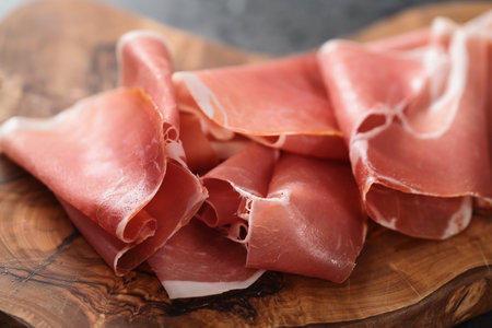 Thin italian prosciutto slices on olive wood board on conctere backgroundの写真素材