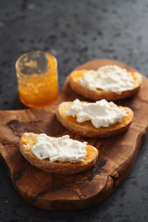 Ciabatta slices with orange marmalade and ricotta on olive boardの写真素材