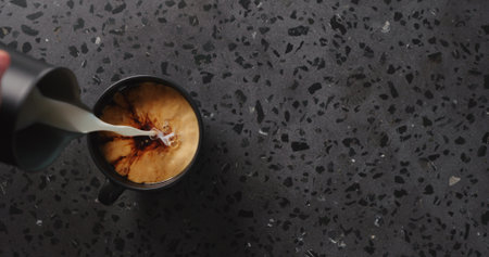 pour cream into black coffee in black cup on concrete background top view